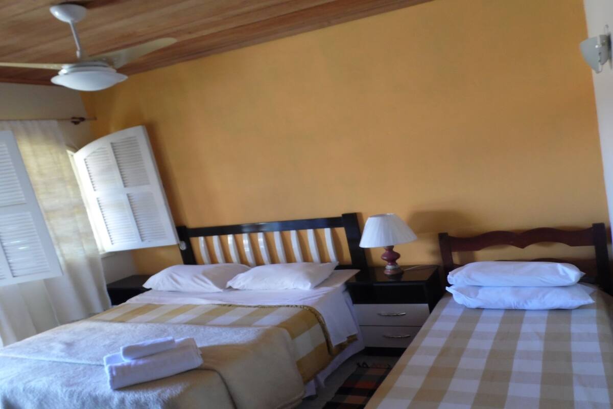 A hotel room with two beds, a wooden ceiling, and a window with blinds.