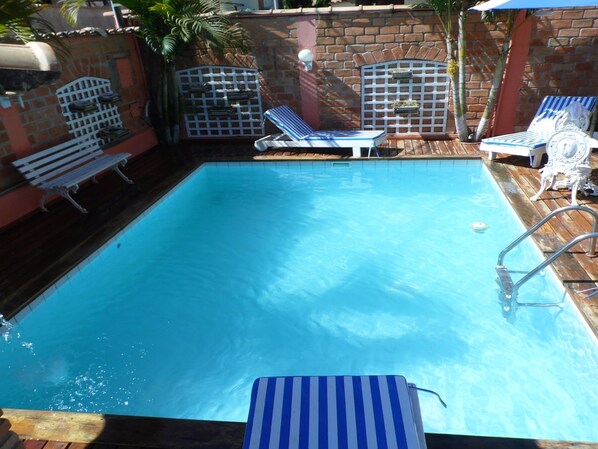 A rectangular swimming pool with a wooden deck and two lounge chairs. - Pousada Brilho Da Serra (Tiradentes)