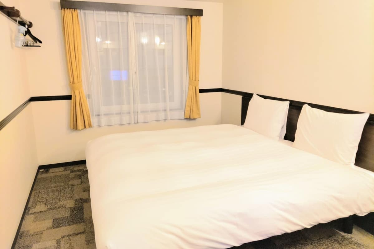Una habitación de hotel con una cama grande, una ventana con cortinas translúcidas y un perchero en la pared.