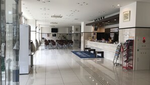 Un vestíbulo amplio con un mostrador de recepción, zona de estar y un camino despejado hacia los ascensores.