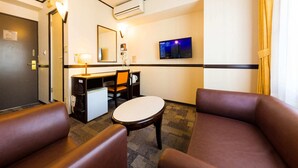Habitación de hotel con escritorio, silla, mesita pequeña, sofá, televisor y aire acondicionado.