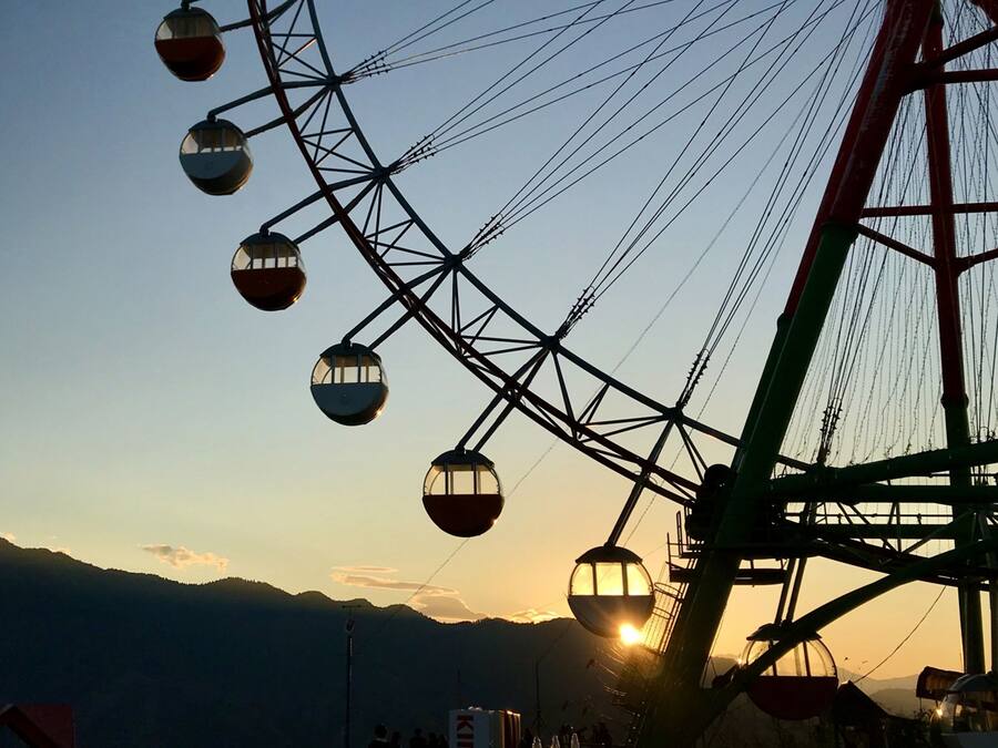 A cable car system with multiple gondolas, a large metal structure, and a mountainous backdrop during sunset.