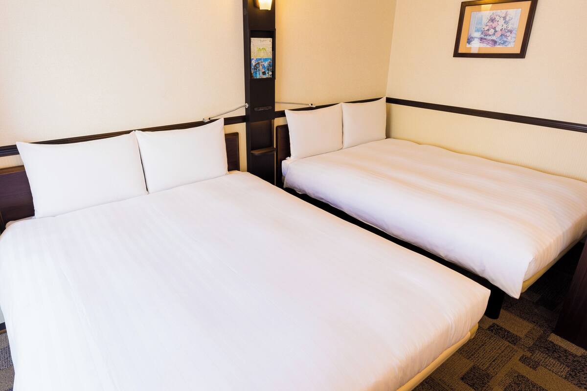 Una habitación de hotel con dos camas individuales, una mesita de noche, una lámpara de pared y un cuadro enmarcado.