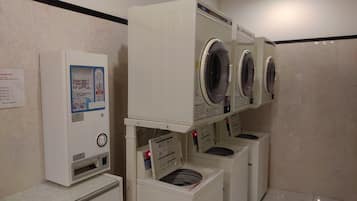 Un cuarto de lavandería con varias lavadoras y secadoras, un terminal de pago y un tablón de anuncios.