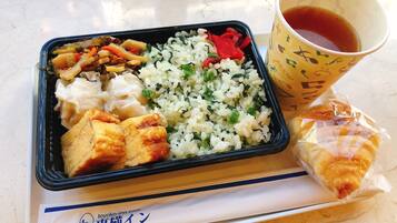 Comida que incluye arroz, verduras, tofu y un pastel, servida en una bandeja junto a una taza de té.