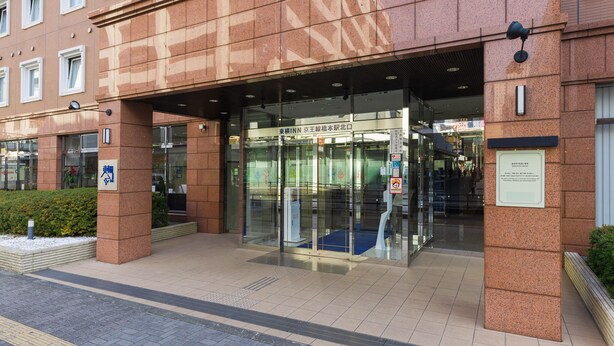 Entrada de hotel con puerta de vidrio, un letrero sobre la puerta y un pequeño espacio exterior con una jardinera.