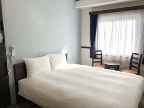A hotel room with a bed, a small table, two chairs, a window with curtains, and a wall-mounted thermostat. - Toyoko Inn Okayama-eki Higashi-guchi (Okayama)