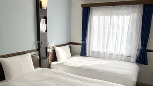 Quarto de hotel com duas camas, uma janela com cortinas azuis e uma mesinha de cabeceira.