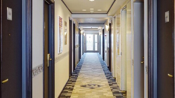 Corredor de hotel com carpete estampado, portas em ambos os lados e vista para o restante do corredor.