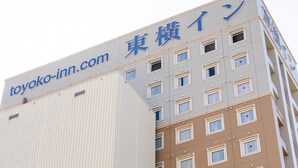 Um hotel com uma placa indicando toyoko-inn.com e caracteres japoneses. Possui vários andares com janelas e fachada bege.