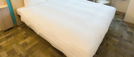 A hotel room with a large bed, a bedside table, a chair, a small round table, and a window with curtains.