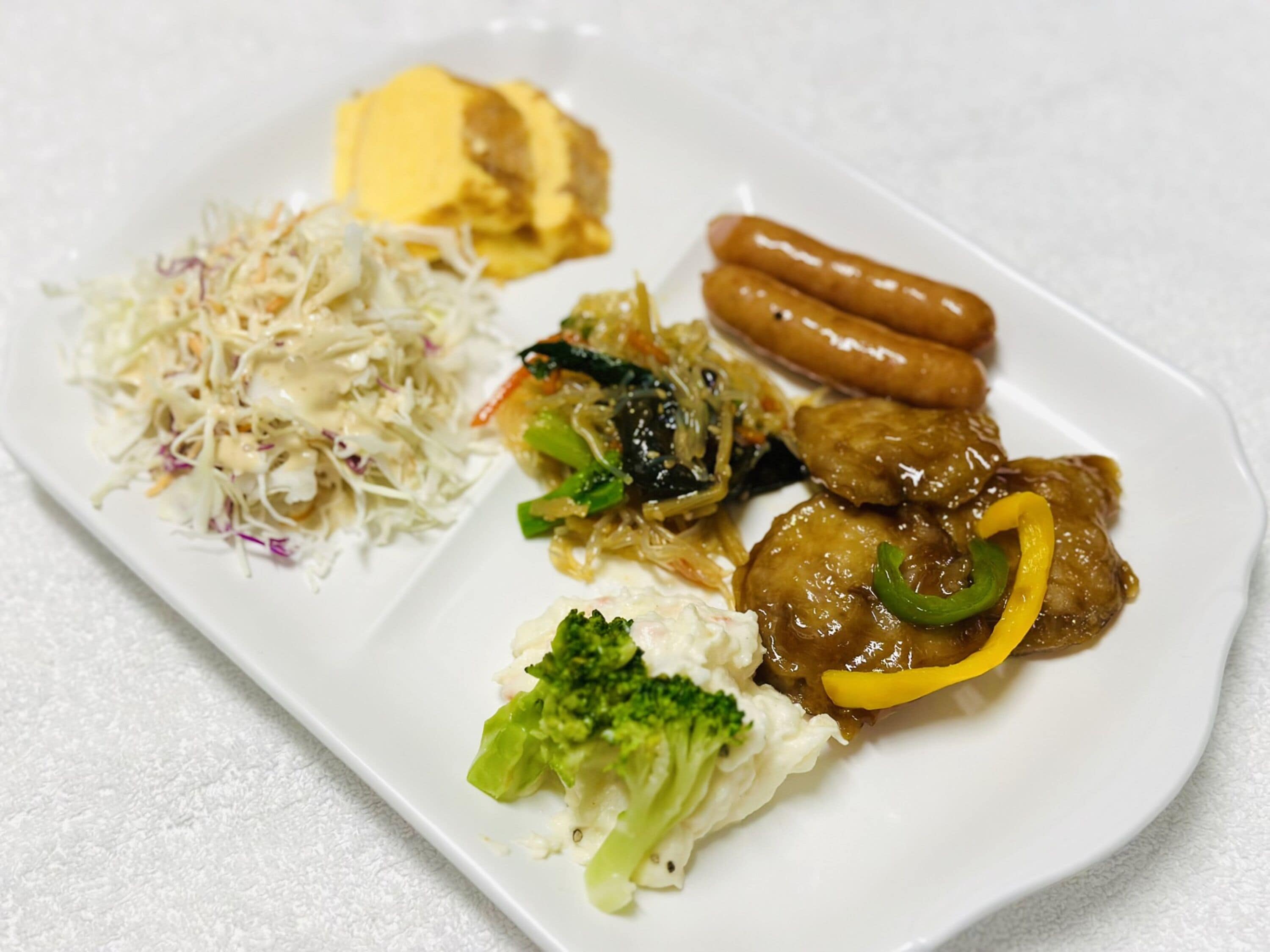 A plate with various dishes including sausages, meatballs, coleslaw, and vegetables.