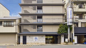 Un hôtel à plusieurs étages, de style architectural japonais traditionnel, avec une façade recouverte de carreaux et une entrée bien visible, dotée d’un socle en pierre.