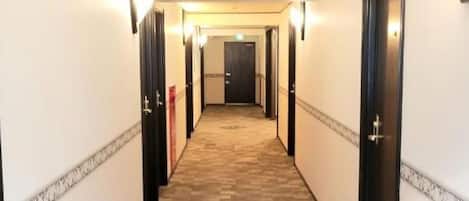 A hotel hallway with carpeted floors, doors on both sides, and wall-mounted lighting.