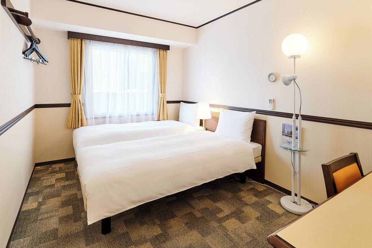 Une chambre d’hôtel avec un lit, un bureau, une lampe et une fenêtre avec des rideaux.