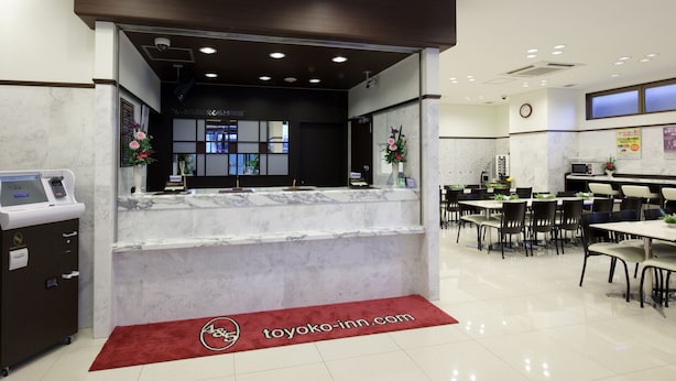 A hotel reception area with a marble counter, a digital kiosk, and a red carpet with the hotel logo. - Toyoko Inn Chiba Station Higashi (Chiba)