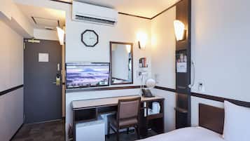 A hotel room with a bed, desk, chair, and a television displaying a mountainous landscape.