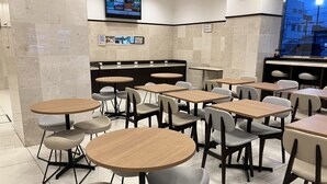 A clean, modern dining area with round tables and chairs, a television screen on the wall, and a clock. - Toyoko Inn Ise Matsusaka Ekimae (Matsusaka)