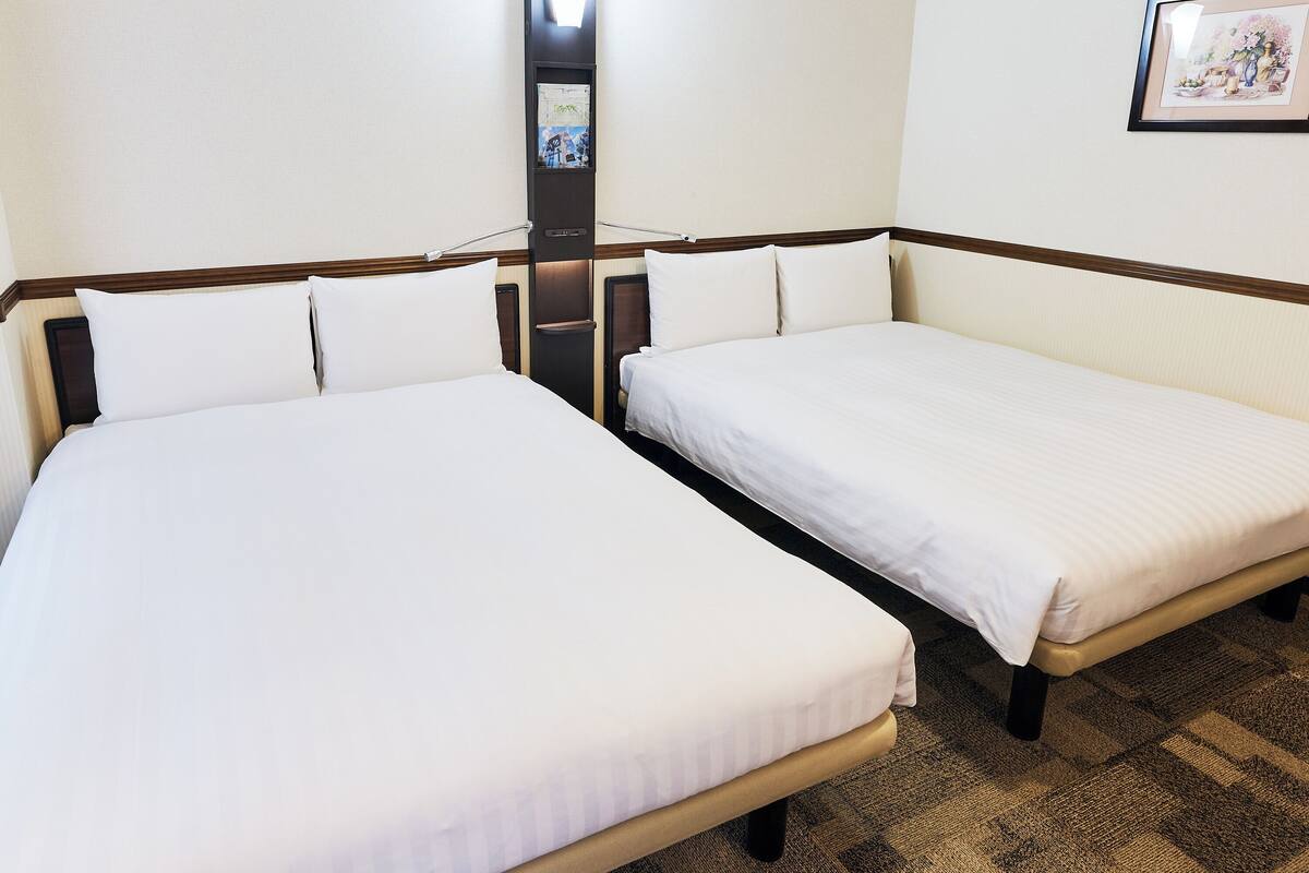 A hotel room with two single beds, a small table, and a wall-mounted TV.