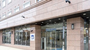 A building entrance with a glass door, a sign with Japanese characters, and a tiled pavement.