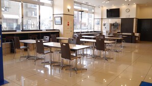 A spacious cafeteria with multiple tables and chairs, large windows, and a kitchen area.