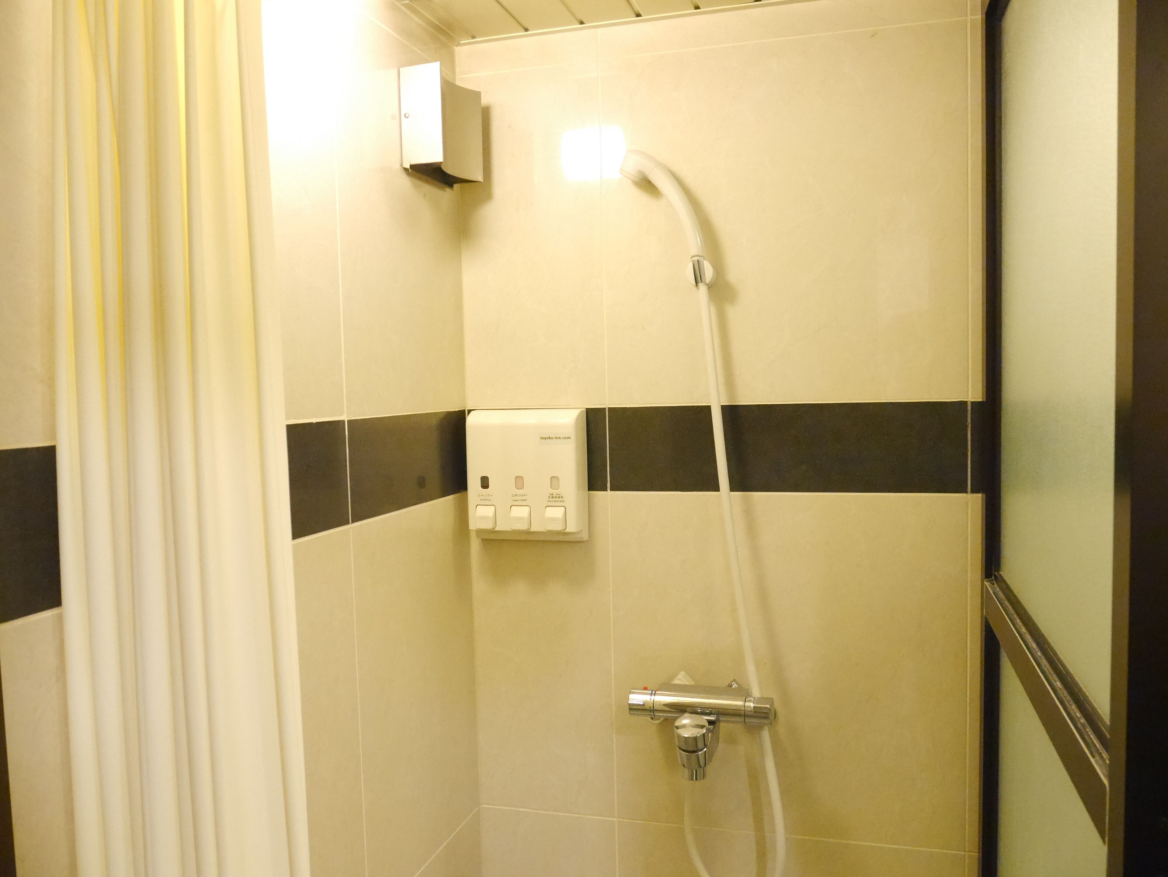 A shower with a handheld showerhead, a wall-mounted control panel, and a tiled floor with a black stripe.