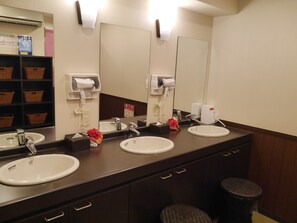 A bathroom with two sinks, a mirror, a hand dryer, a trash can, and wicker baskets on shelves. - Toyoko Inn Gumma Ota Station Minami (Ota)