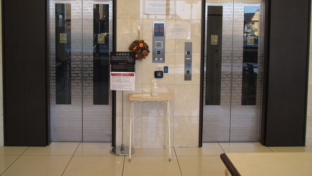 An elevator area with two elevators, a small table with a bottle, and a sign with instructions.