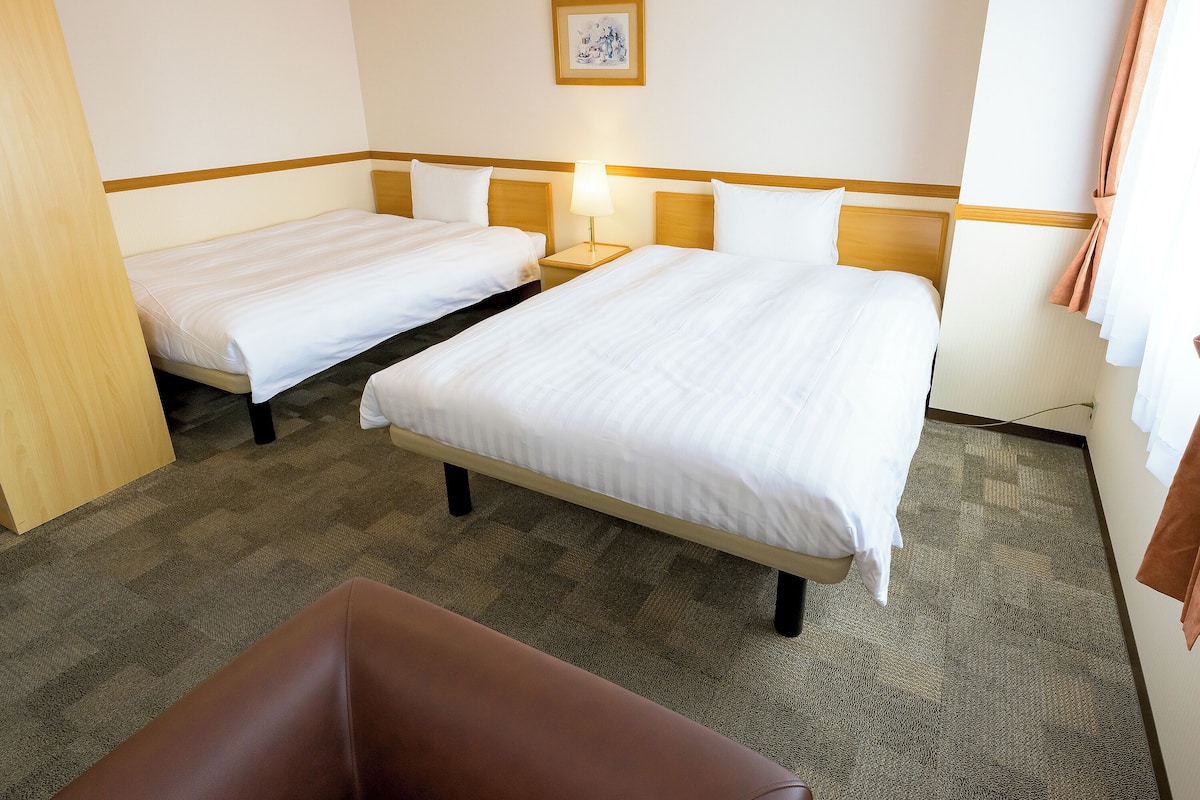 Ein Hotelzimmer mit zwei Einzelbetten, einem braunen Sessel und einem kleinen Tisch.