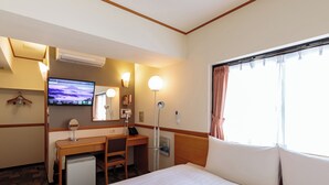 A hotel room with a bed, desk, chair, TV, and a window with curtains.
