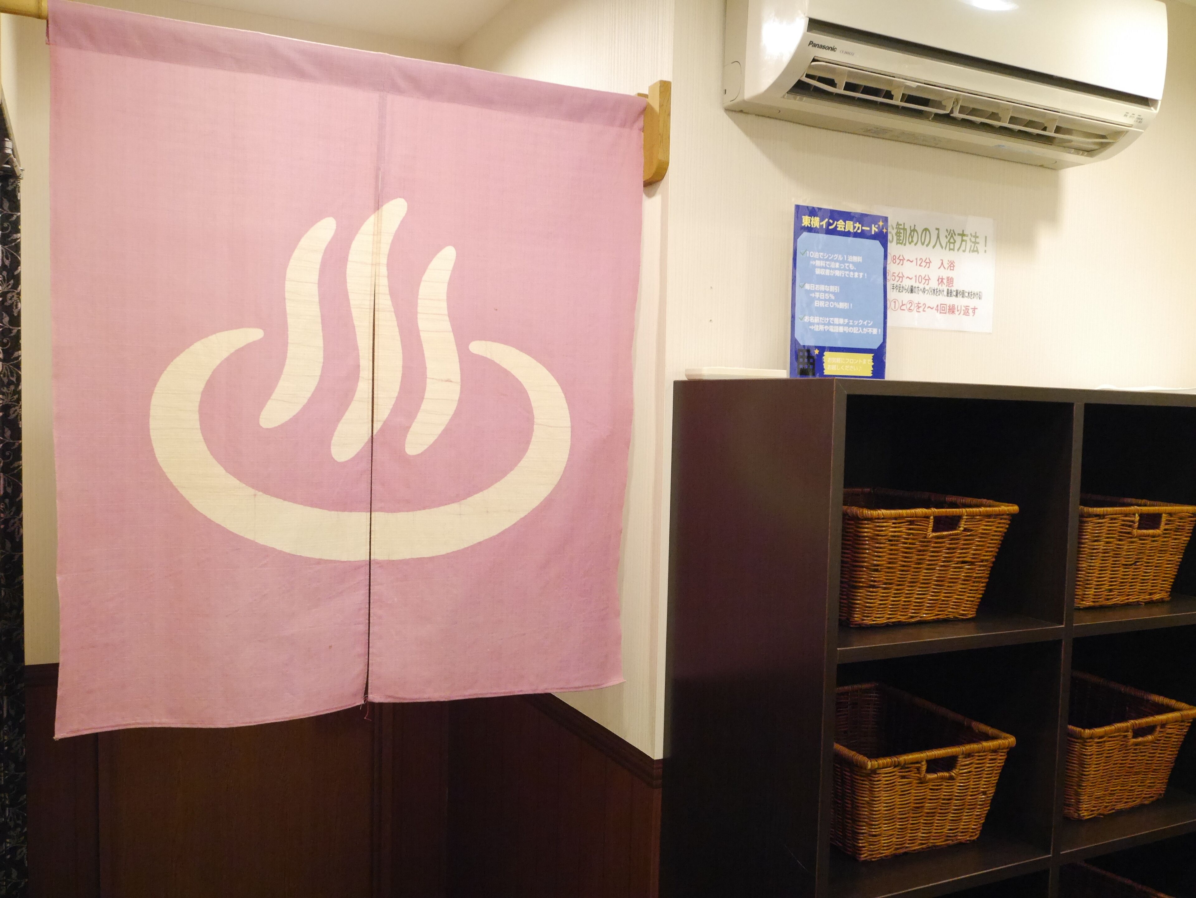 A room with a pink towel featuring a white symbol, a wall-mounted air conditioner, and wicker baskets on shelves.