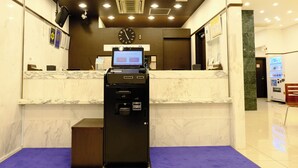 Zona d'entrada d'un hotel amb un panell digital, un rellotge i una màquina expenedora.