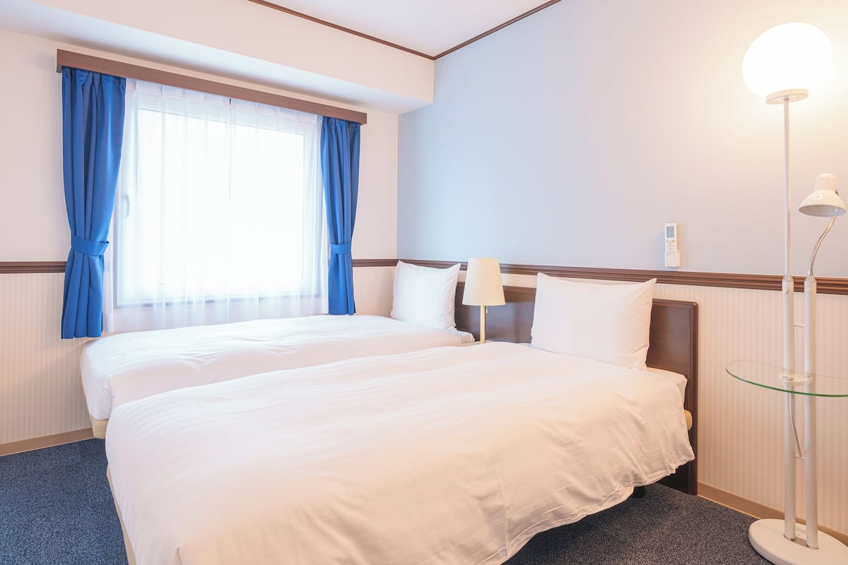 Une chambre d’hôtel avec un grand lit, une table de chevet avec une lampe et une fenêtre avec des rideaux.