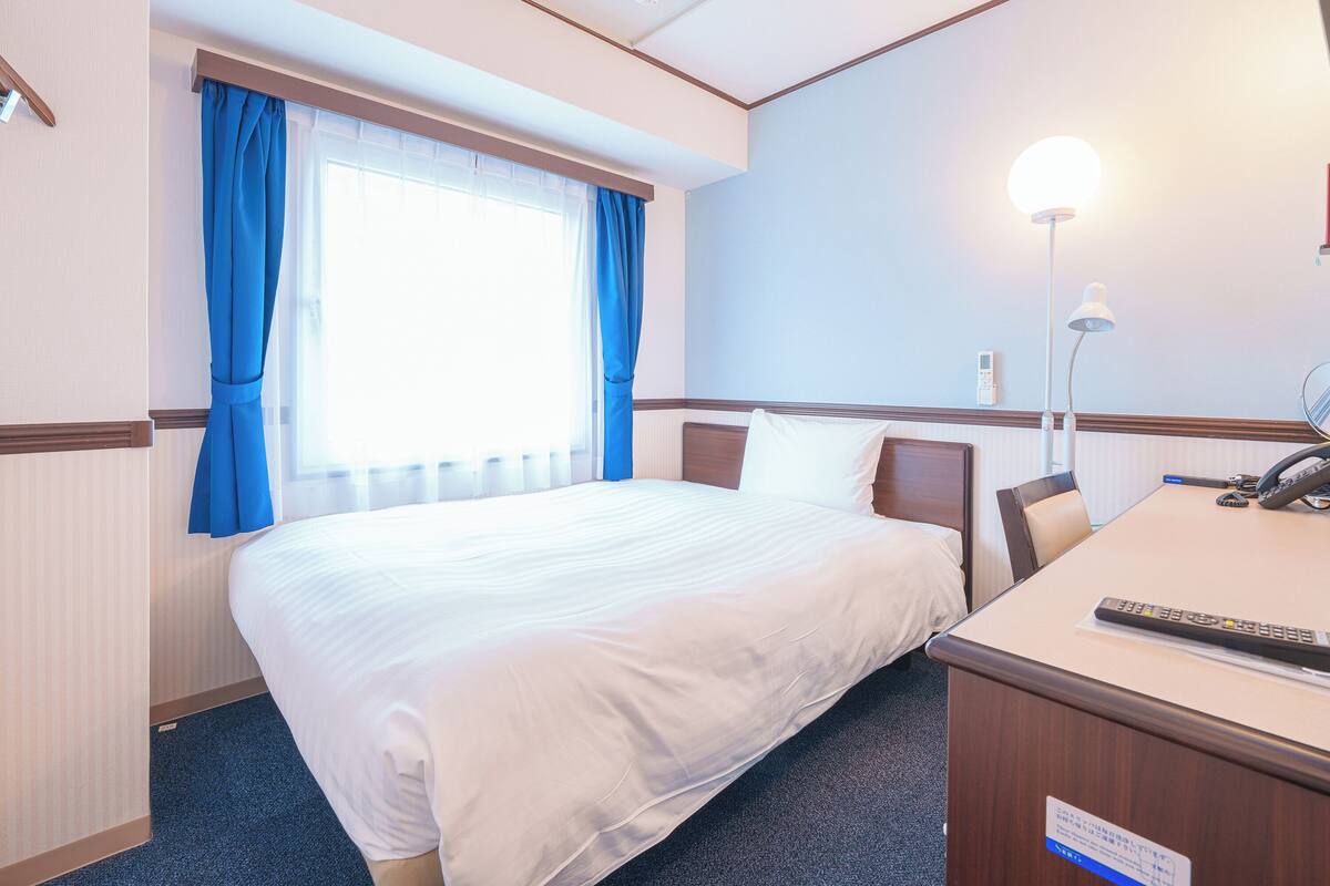 Une chambre d’hôtel avec un lit, un bureau doté d’un téléphone et une lampe.