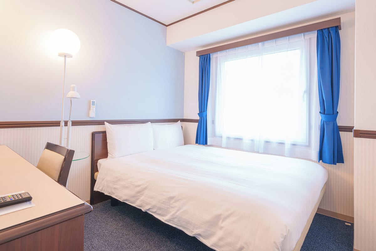 Une chambre d’hôtel avec un lit, un bureau, une lampe et une fenêtre avec des rideaux.