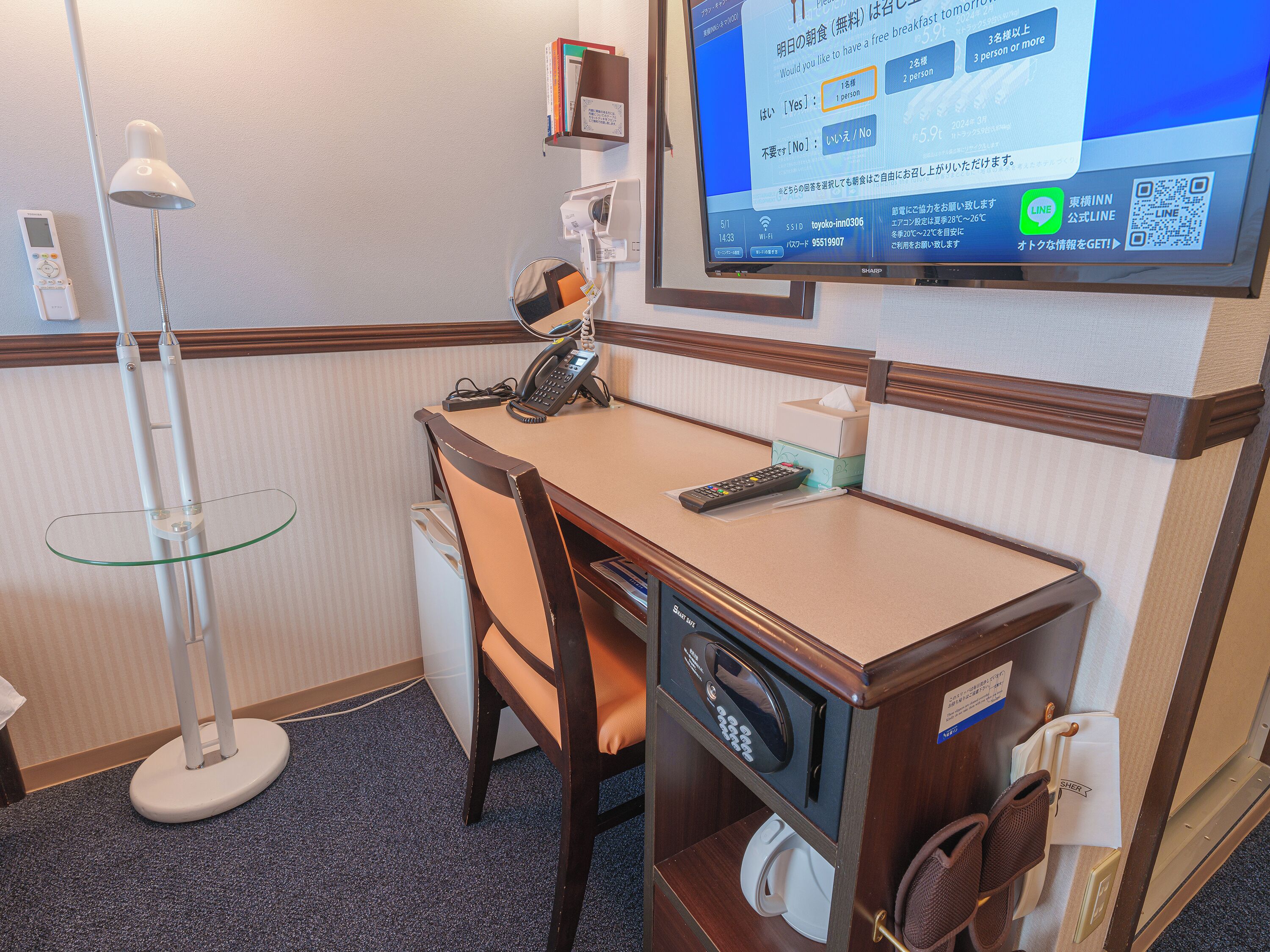 A hotel room with a desk, chair, lamp, and a television displaying a menu.