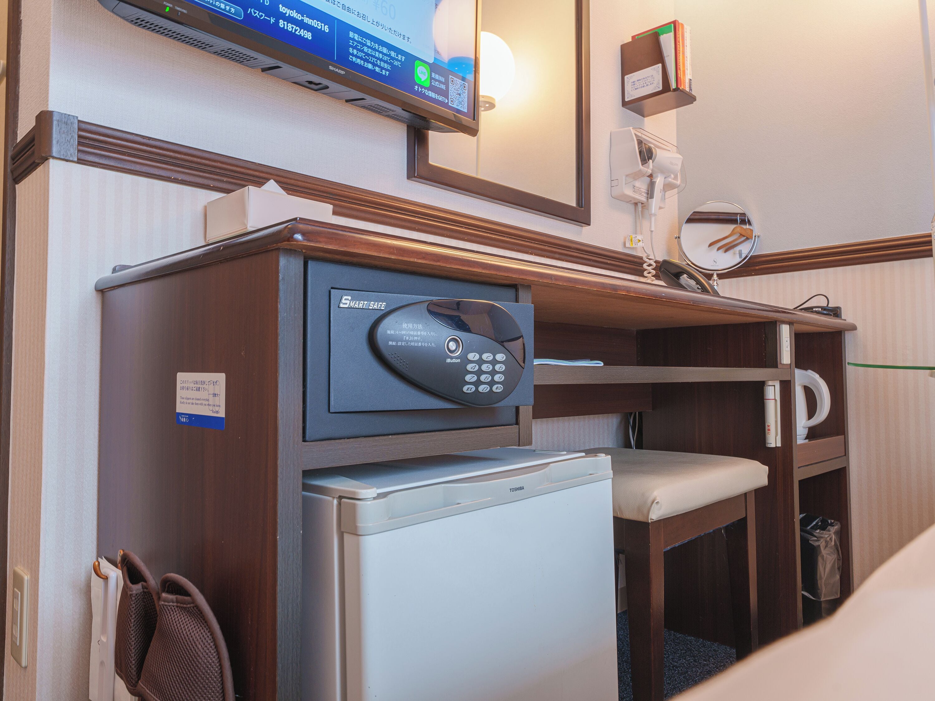 A hotel room with a minibar, a refrigerator, a desk with a telephone, and a television mounted on the wall.