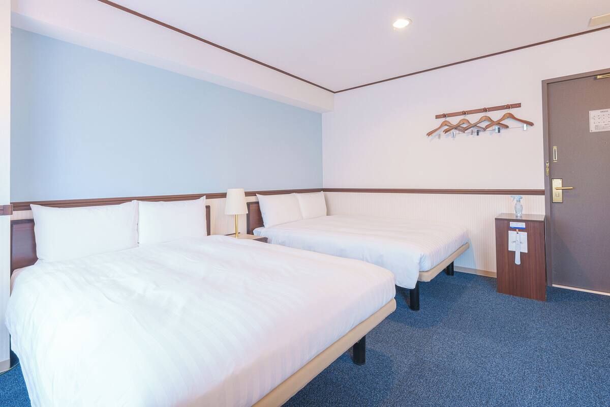 Une chambre d’hôtel avec deux lits, une moquette bleue, une porte en bois et un porte-manteau fixé au mur.