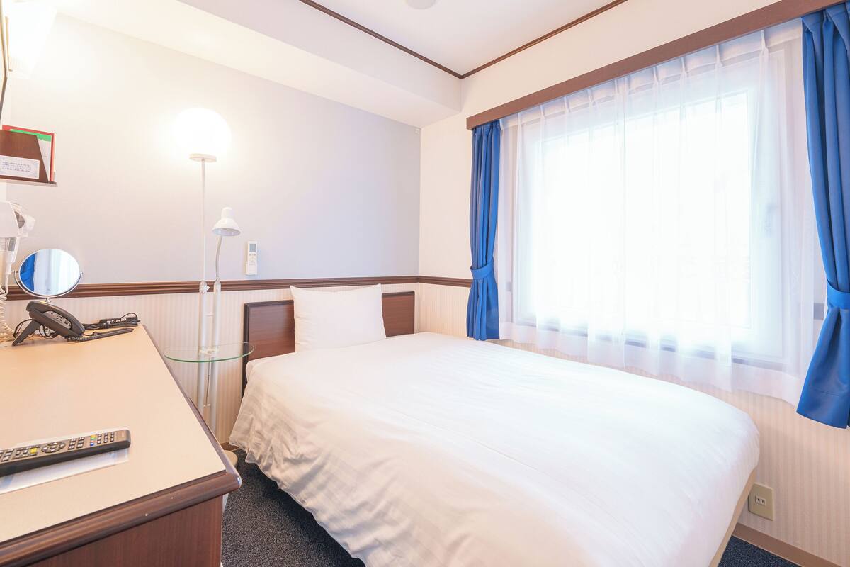 Une chambre d’hôtel équipée d’un lit, d’une table de chevet, d’une lampe et d’un téléphone.