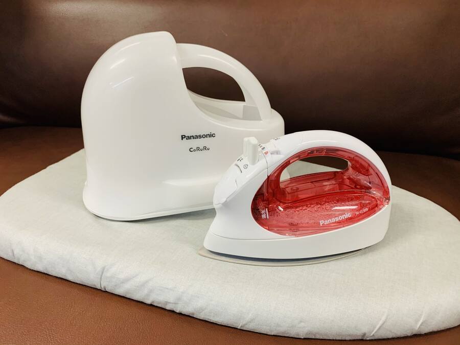 A white Panasonic iron with a red water tank on a white cushion on a brown leather couch.