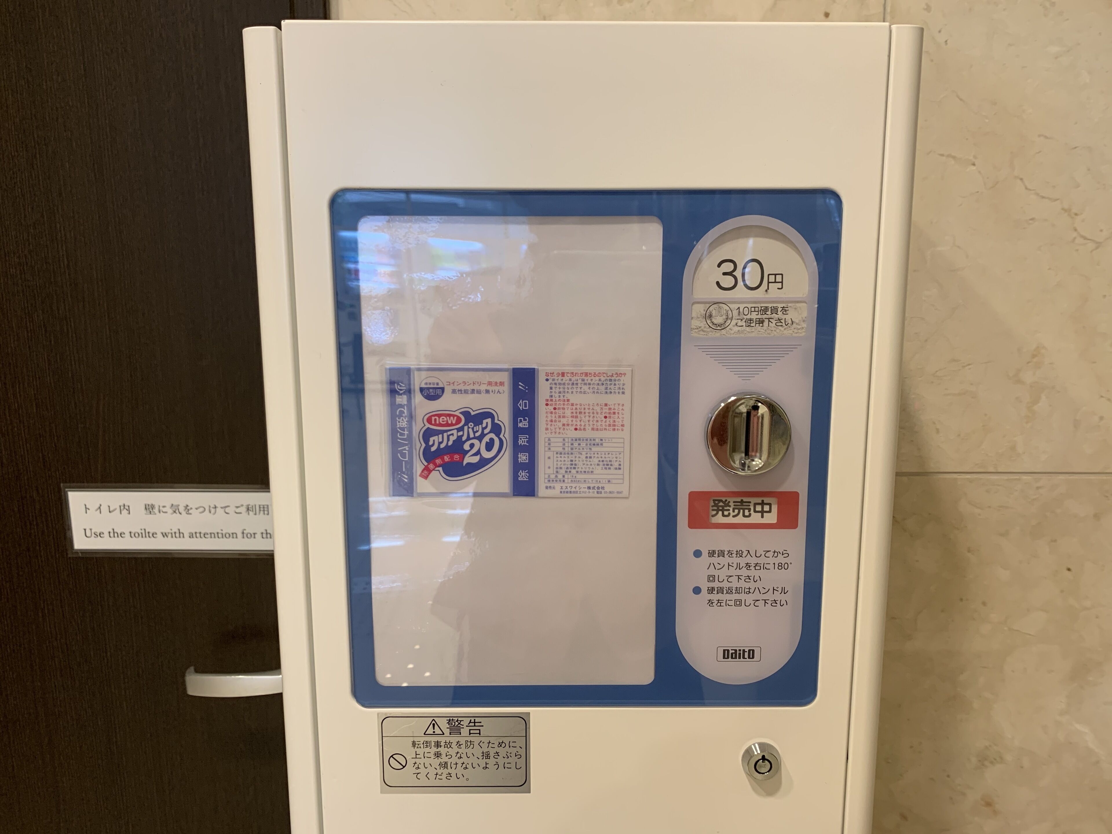 A public toilet with a blue and white color scheme, a 30 yen coin slot, and a sign instructing to use the toilet with attention for health.