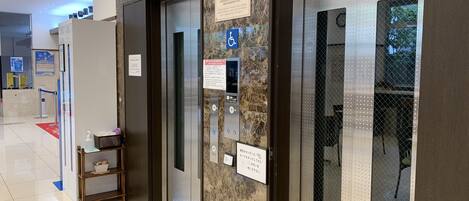 An elevator area with marble walls, a digital screen, and informational signs.
