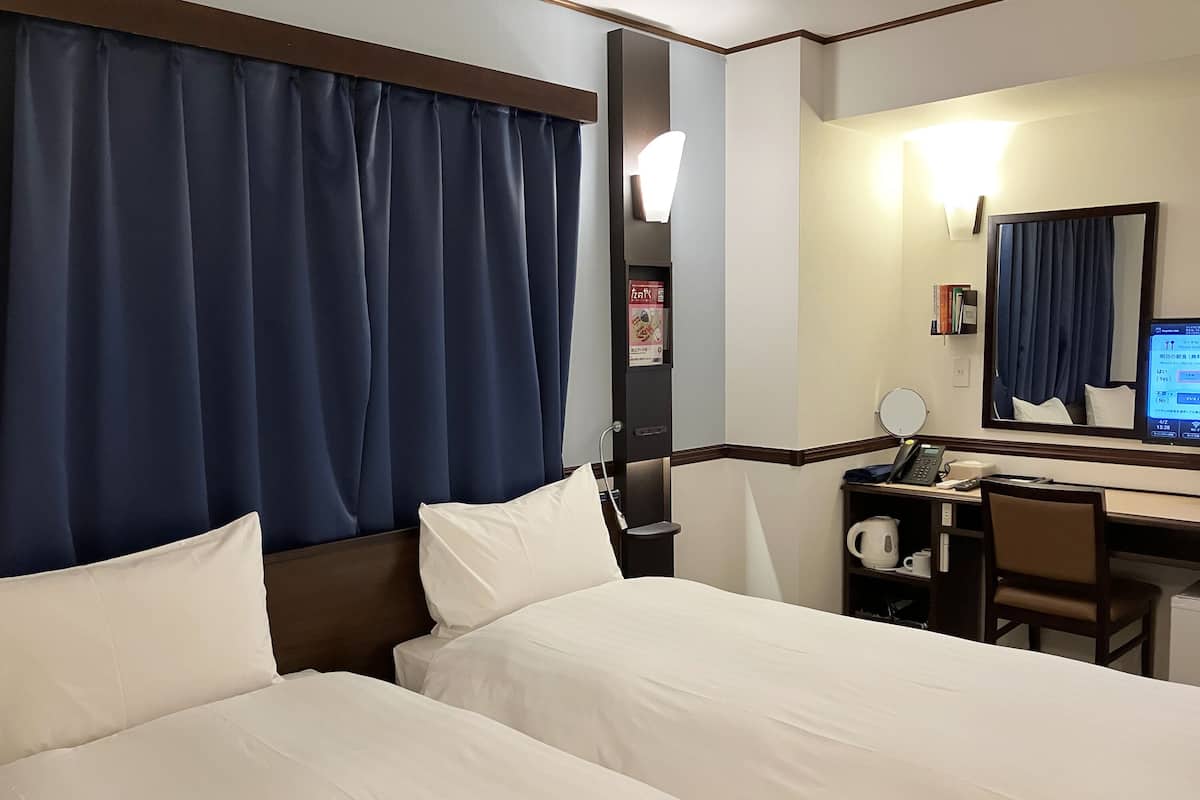 Habitación de hotel con dos camas, un escritorio, una silla, una computadora y un espejo.