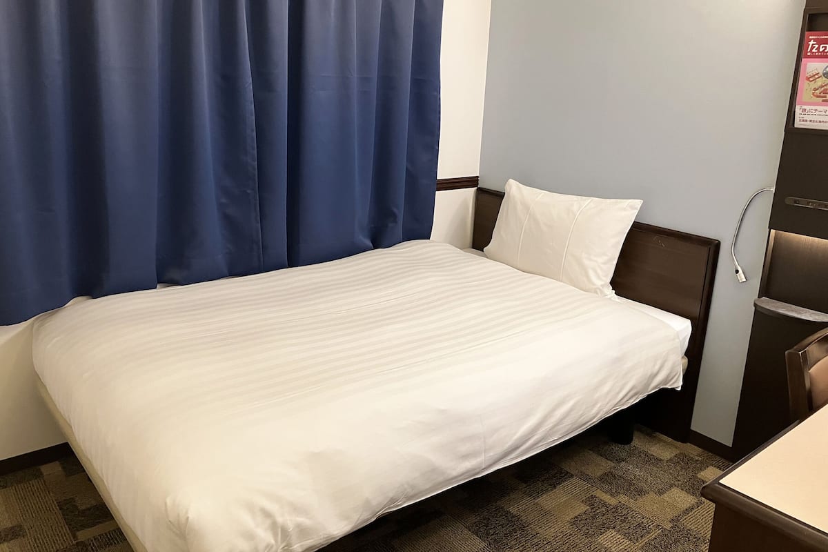 Una habitación de hotel con una cama, una mesita de noche, una lámpara y un televisor instalado en la pared.
