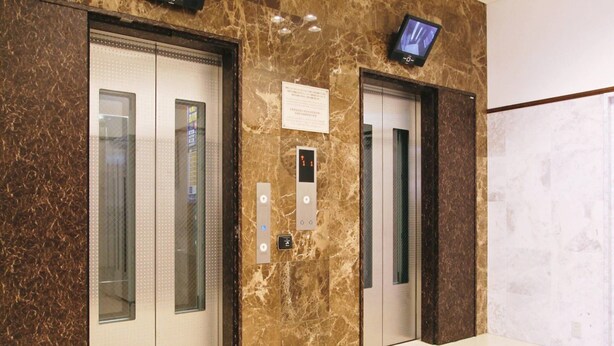 Deux ascenseurs aux parois en marbre, un écran numérique et un panneau indiquant les équipements facilitant l’accès aux personnes à mobilité réduite.