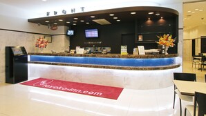 Un espace d’accueil d’hôtel doté d’un comptoir en marbre, d’un écran numérique et d’un tapis rouge sur lequel figure l’adresse du site web de l’hôtel.