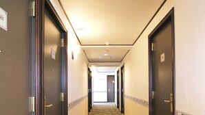Un couloir d’hôtel avec des revêtements de sol en moquette, des portes en bois foncé et des murs de couleur claire.
