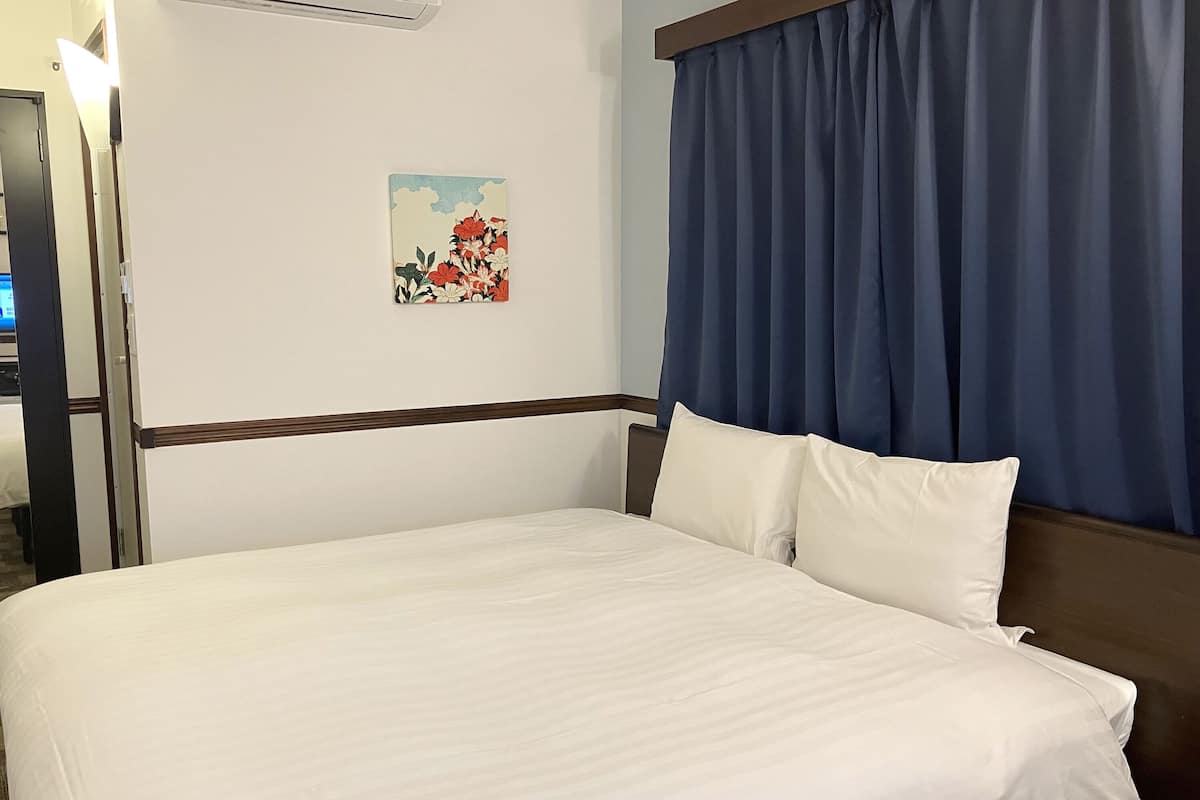Una habitación de hotel con una cama, un cuadro y una ventana con cortinas.