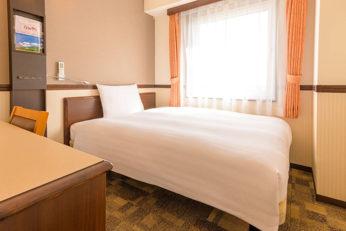 Une chambre d’hôtel avec un lit, un bureau, une chaise et une fenêtre avec des rideaux.