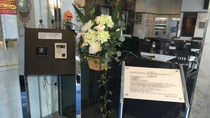 Un espace d’accueil avec un bureau en verre, un arrangement floral et un panneau avec du texte.